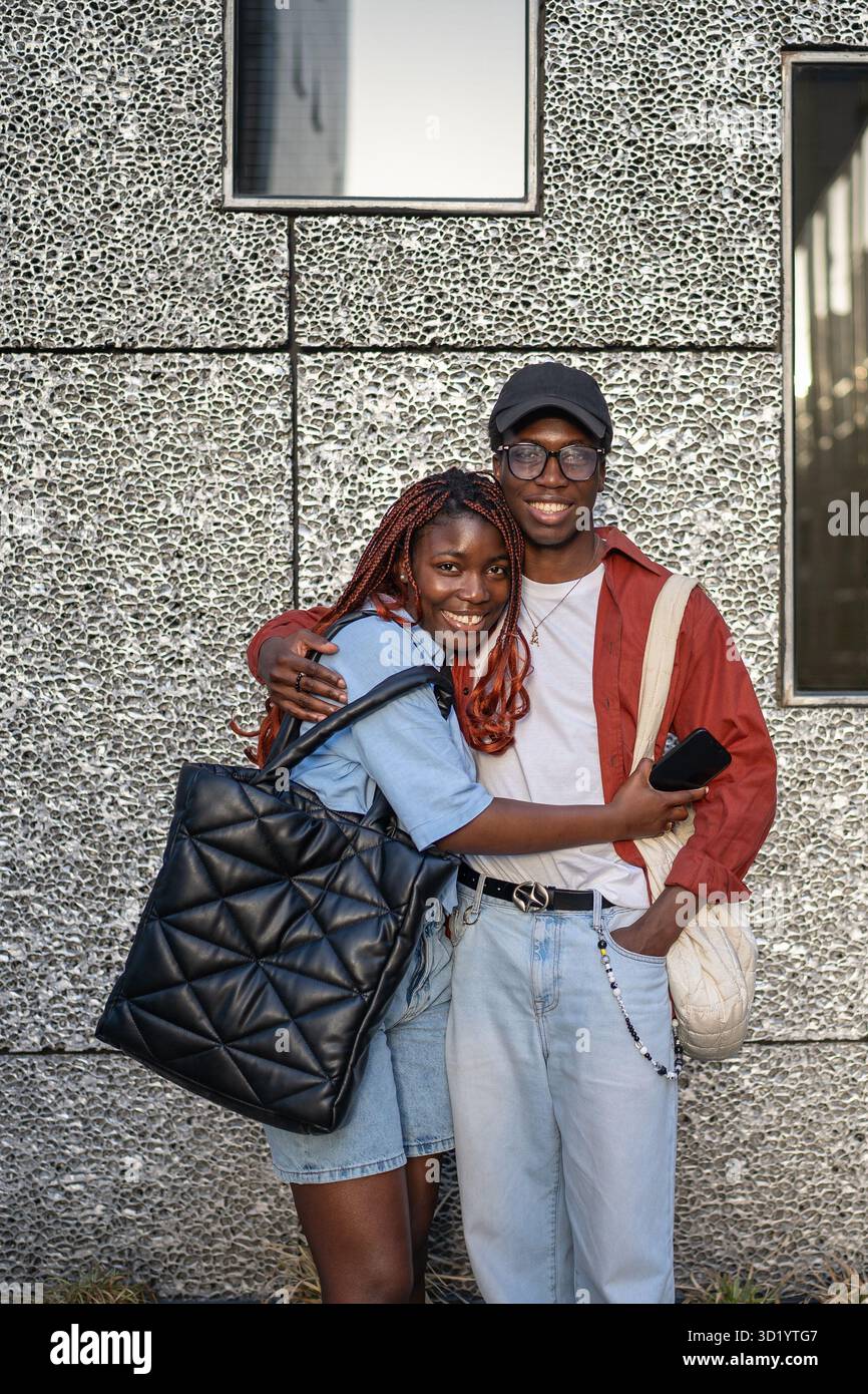 Felici fratelli afro-americani che si ammucchiano, guarda la macchina fotografica con i sorrisi vicino al muro. Passeggiata nel fine settimana Foto Stock