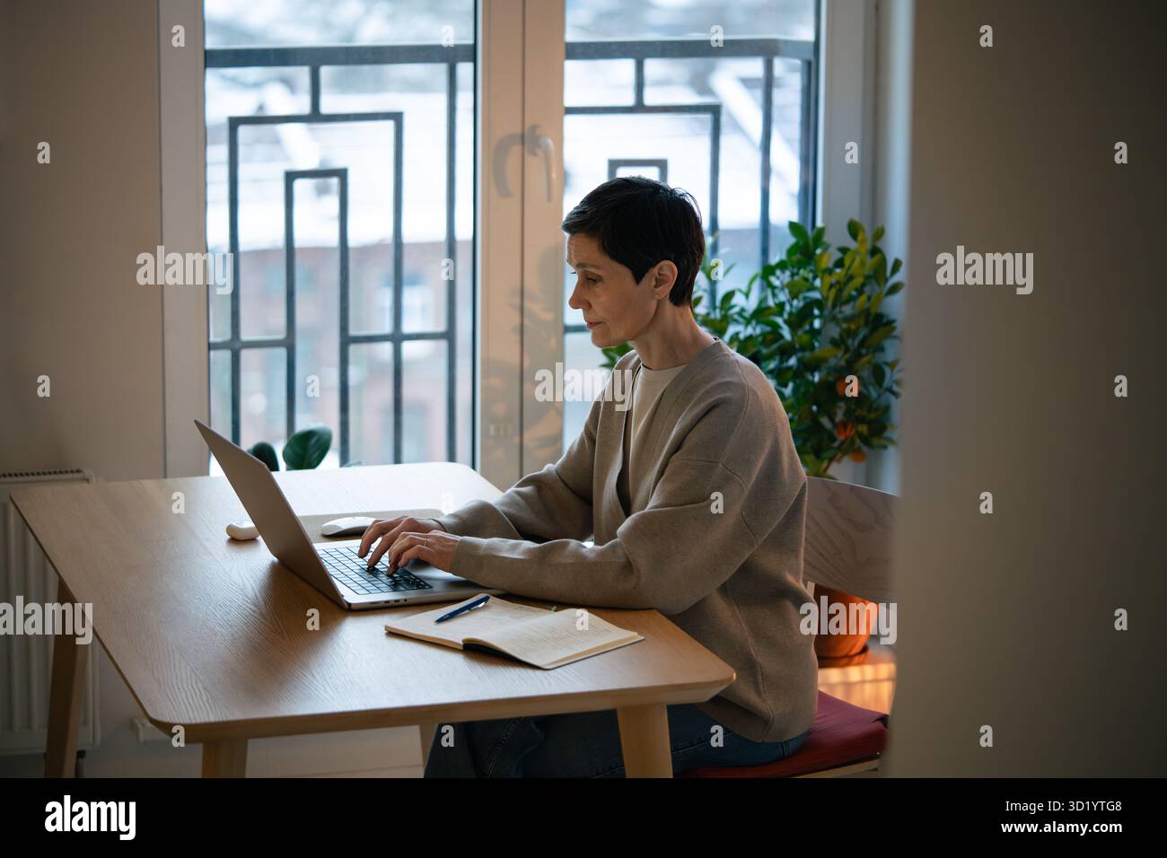 Una donna stanca e concentrata lavora al notebook, prendi appunti a casa. Bilancia lavoro remoto e studio Foto Stock