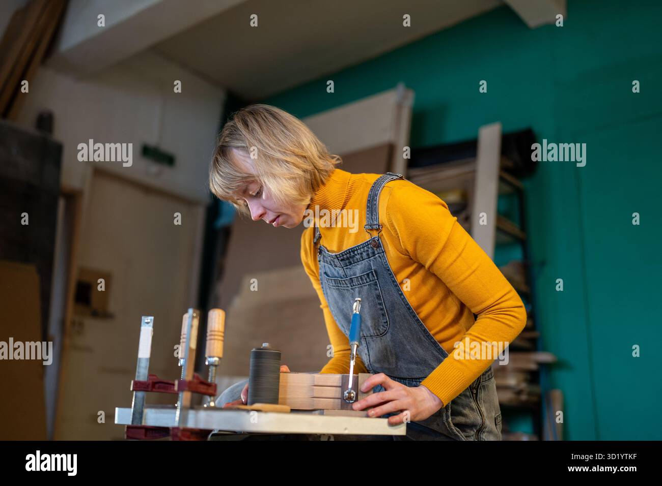 Falegname femminile trasforma il legno su tornio, crea pezzi personalizzati in officina. Manodopera qualificata, ordini personalizzati Foto Stock