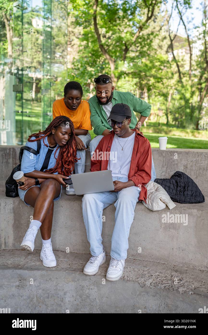 Allegro gruppo multirazziale goditi un film o una videochiamata sul portatile all'esterno. Quattro studenti che si divertono Foto Stock