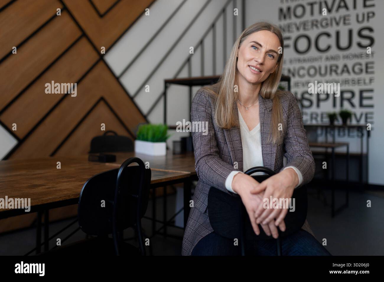 Donna professionista che sorride con fiducia in uno spazio di lavoro moderno con citazioni ispiratrici sulla parete Foto Stock