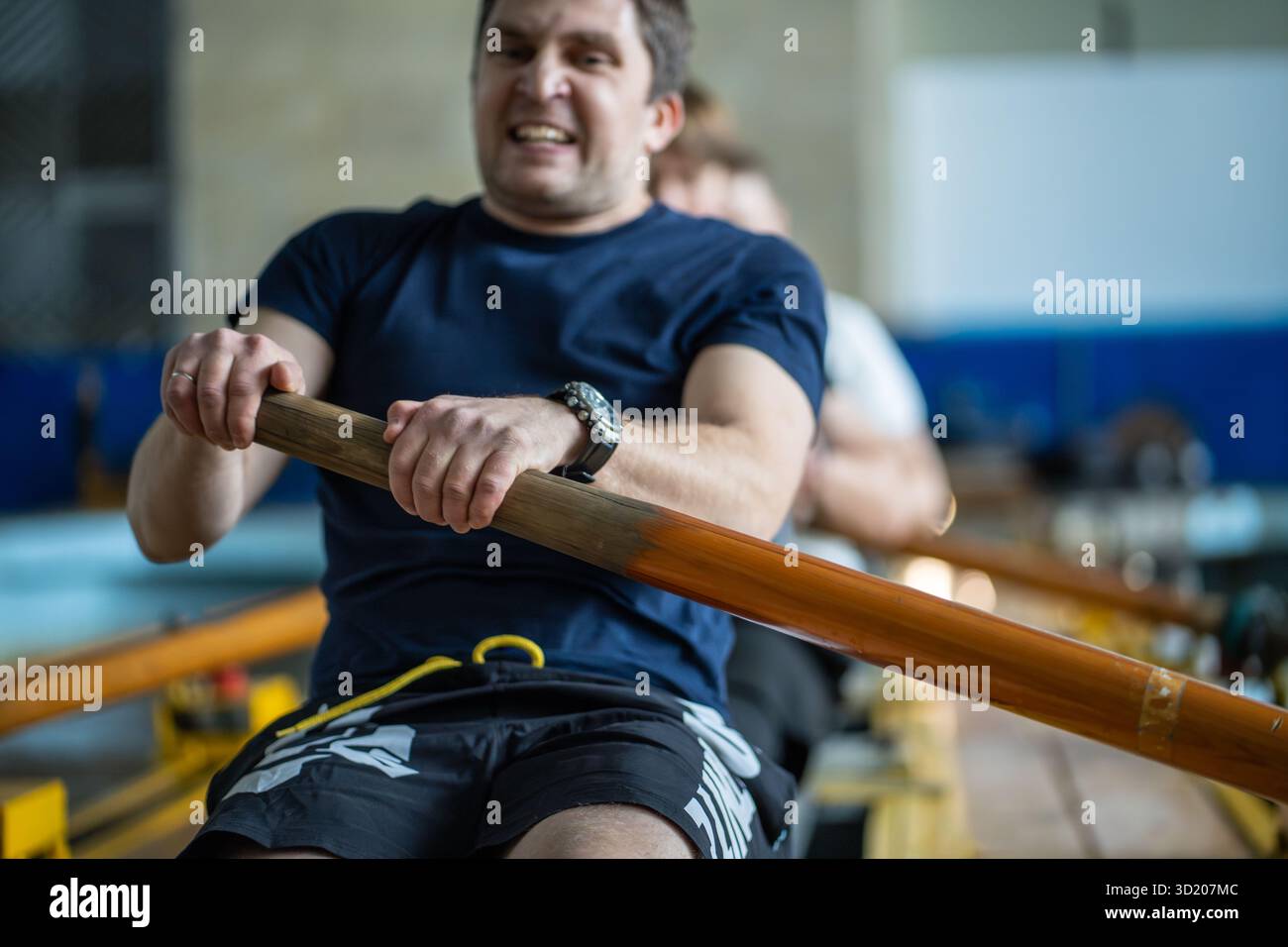 L'atleta stanco e faticoso si fa carico di faticosamente, remando sul simulatore con grinta e determinazione Foto Stock