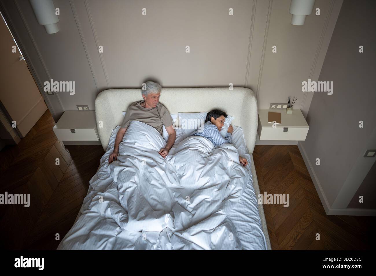Coppia matura in crisi, distanza emotiva evidente mentre discutono a letto, rottura della comunicazione Foto Stock
