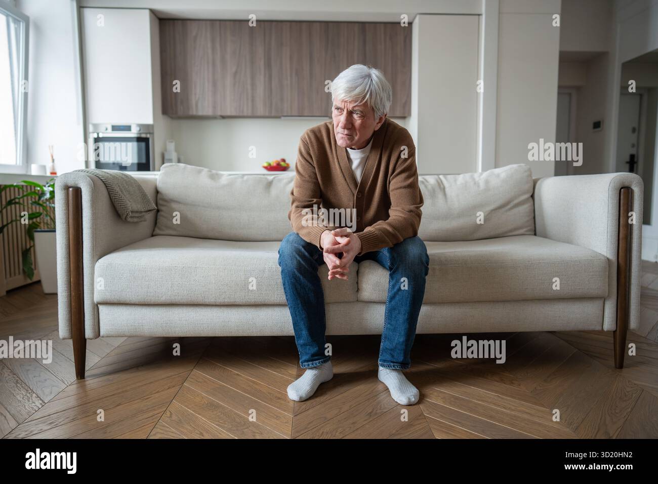 Uomo anziano abbandonato solo si siede perso nel pensiero sul divano con le braccia incrociate, perdita di memoria depressa Foto Stock