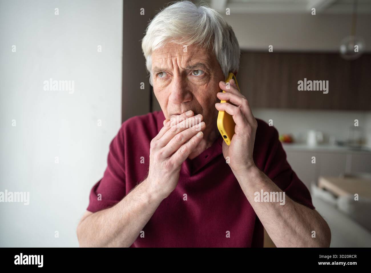 Uomo anziano sospetto con il telefono a casa, preso di mira da truffatori, telemarketing notizie false Foto Stock