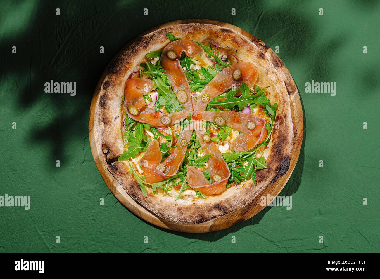 Pizza rustica cotta nel forno a legna condita con rucola fresca e salmone affumicato su sfondo verde Foto Stock