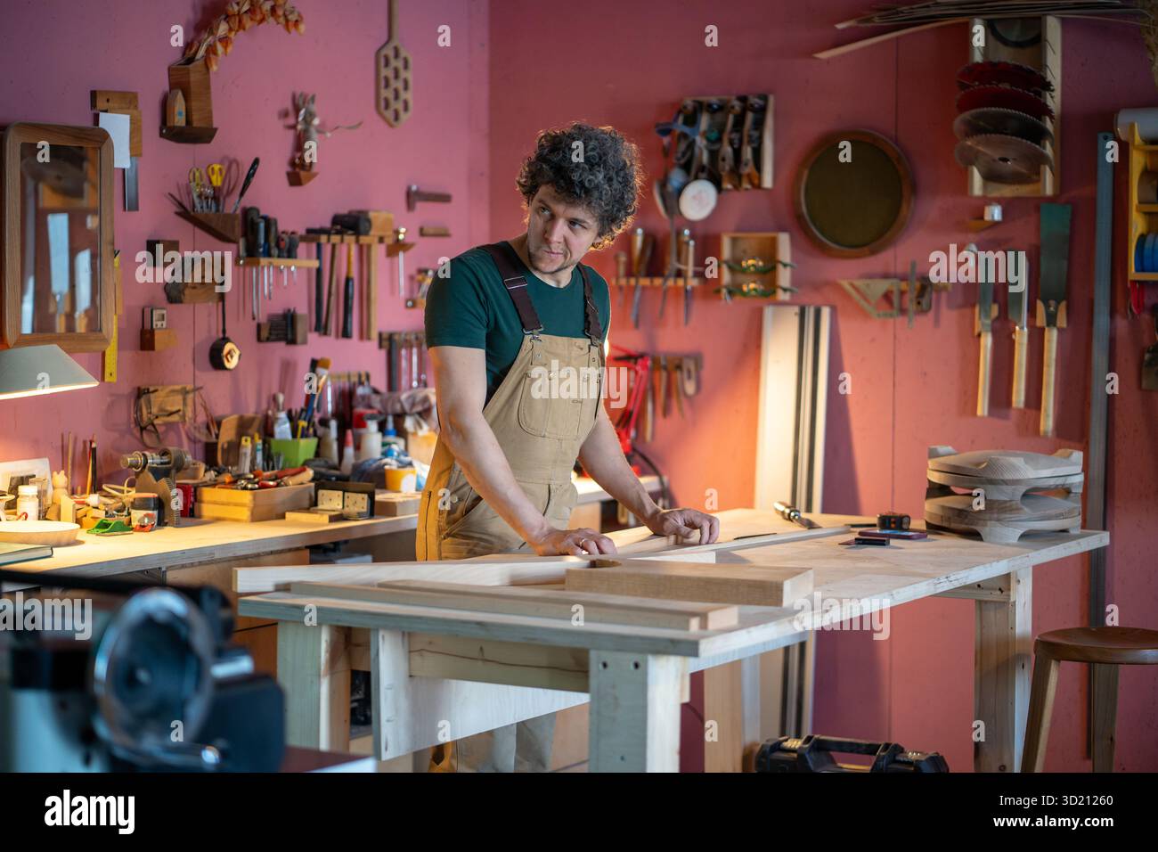Il falegname esperto pianifica l'assemblaggio di mobili alla ricerca di utensili in un'officina di falegnameria molto affollata Foto Stock