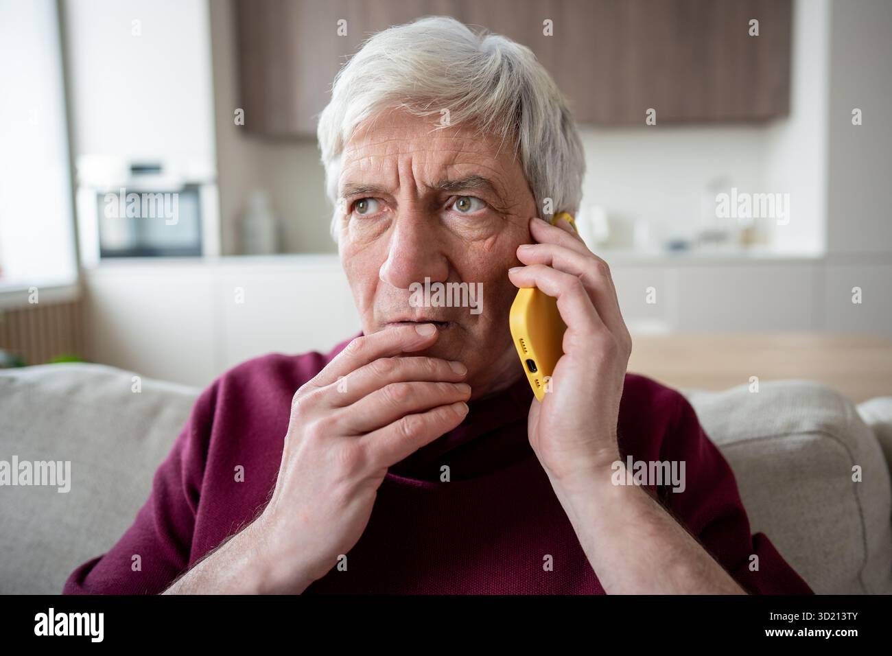 Uomo anziano sospetto con il telefono a casa, preso di mira da truffatori, telemarketing notizie false Foto Stock