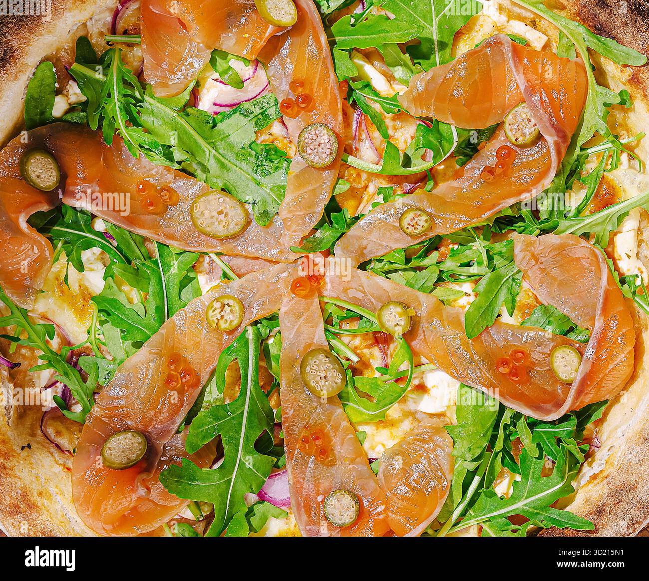 Pizza rustica cotta nel forno a legna condita con rucola fresca e salmone affumicato su sfondo verde Foto Stock