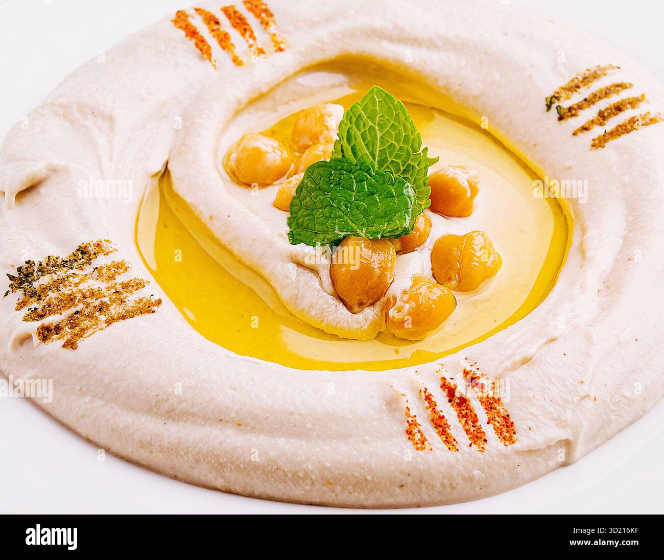 Hummus cremoso servito su un piatto bianco guarnito con ceci e olio d'oliva Foto Stock