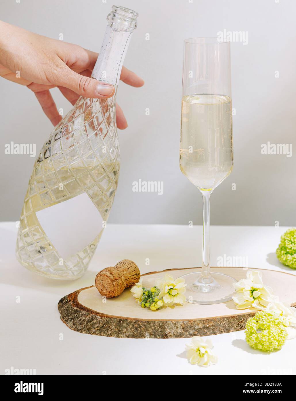 Elegante bevanda frizzante con fiori e sughero su una fetta di legno in un ambiente luminoso Foto Stock