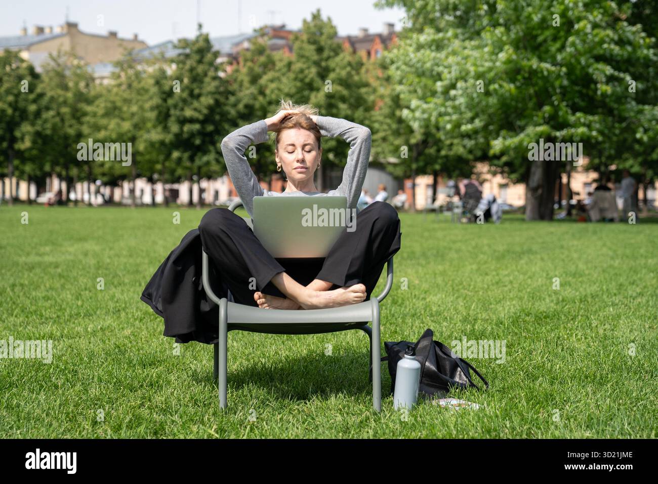 Una donna rilassata riposa con gli occhi chiusi mentre ascolta le lezioni sul laptop nel parco. Scuola online, studio Foto Stock