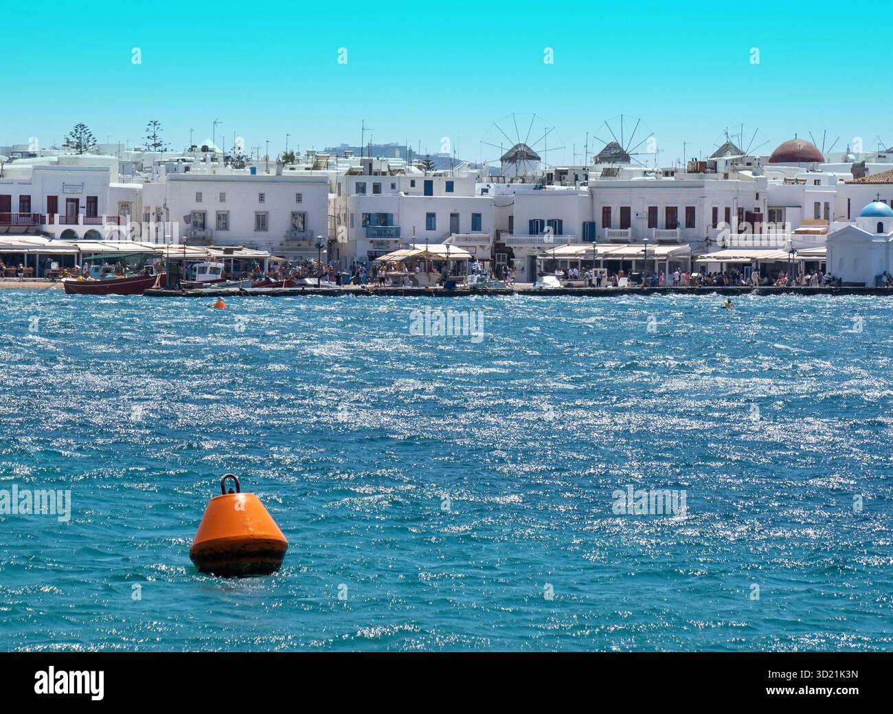 Boa arancione che galleggia nel porto di Mykonos con mulini a vento sullo sfondo Foto Stock