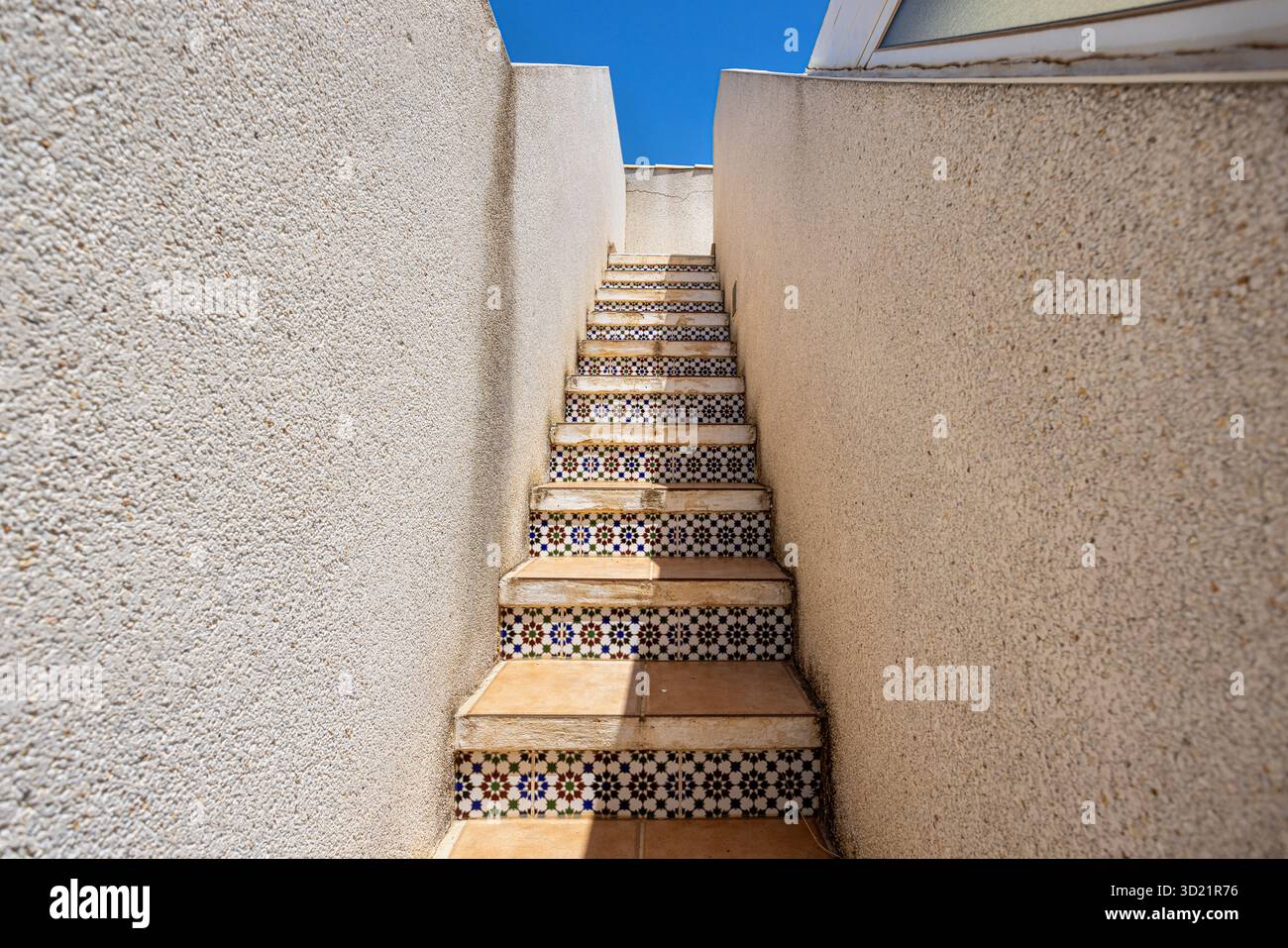 Scale esterne testurizzate con montanti in piastrelle a motivi geometrici e pareti beige sotto il cielo soleggiato Foto Stock