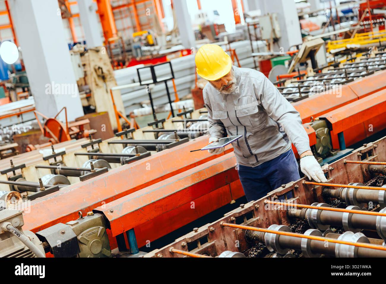 Lavoratore industriale senior professionista in caschi protettivi e macchinari per servizi uniformi in fabbrica Foto Stock