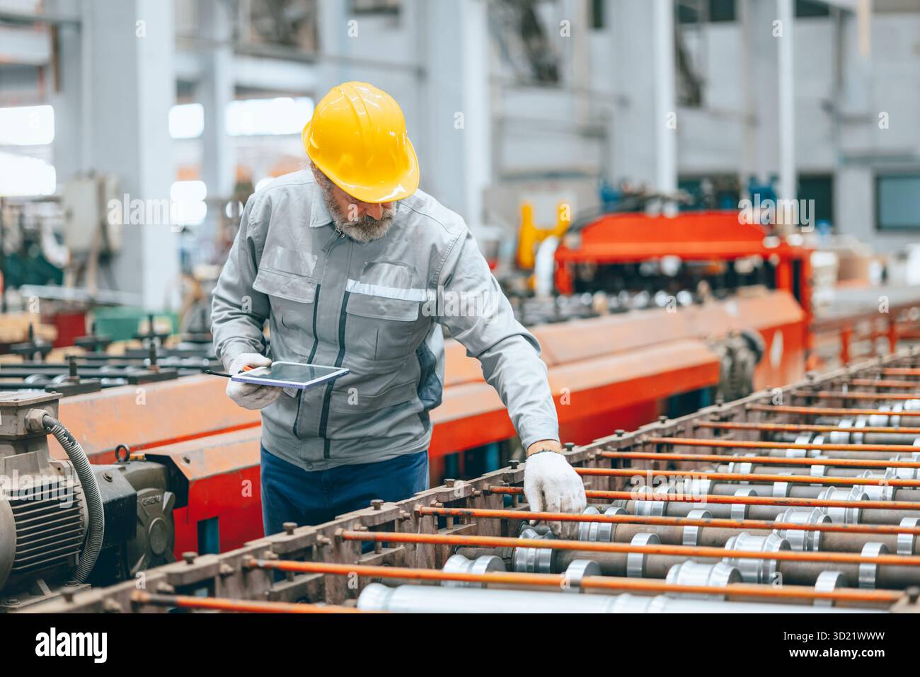 Lavoratore industriale senior professionista in caschi protettivi e macchinari per l'assistenza uniforme in fabbrica, tecnico esperto addetto alla manutenzione di macchinari pesanti Foto Stock