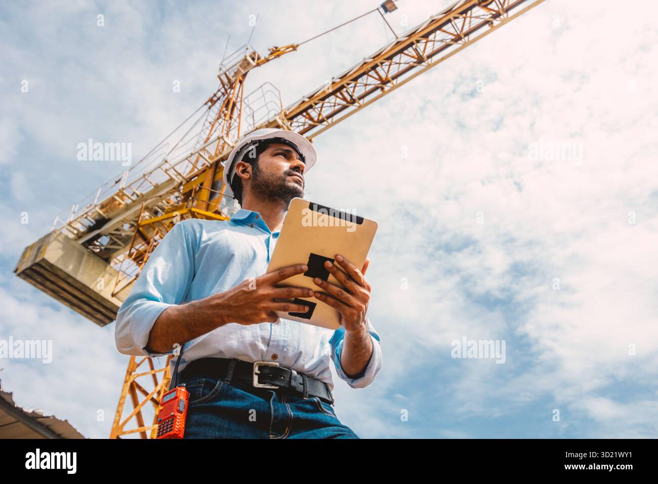 Ingegnere edile indiano operaio operazioni di controllo del cantiere. Foreman aziona una gru a torre che tiene il tablet. Foto Stock