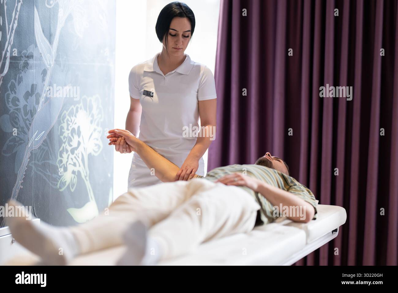 Terapeuta che esegue l'allungamento del braccio. Una terapeuta femminile esegue una tecnica di allungamento del braccio su un paziente di sesso maschile disteso su un letto di trattamento. Foto Stock