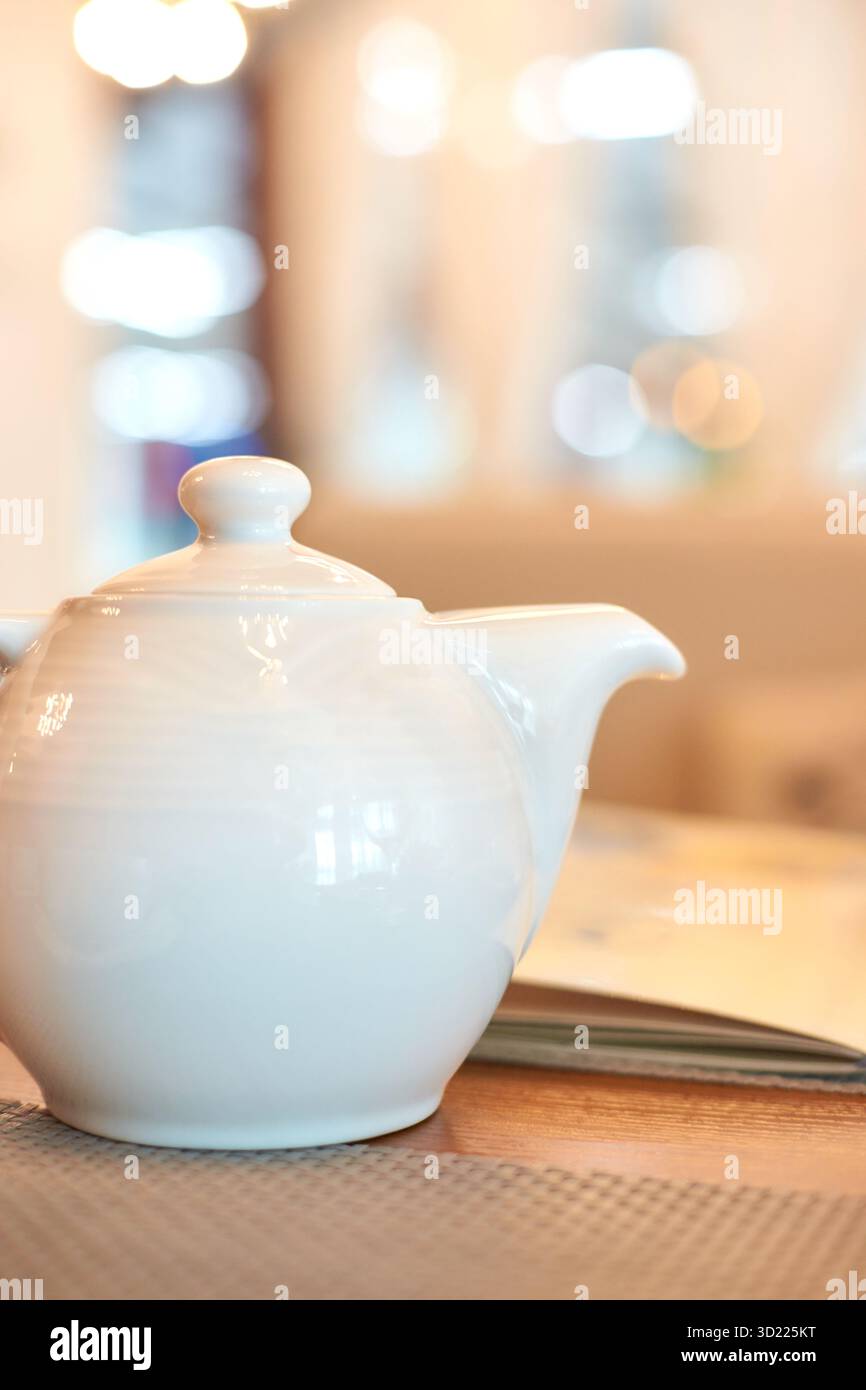 Elegante teiera bianca su un tavolo di legno in un ambiente da caffe' luminoso Foto Stock