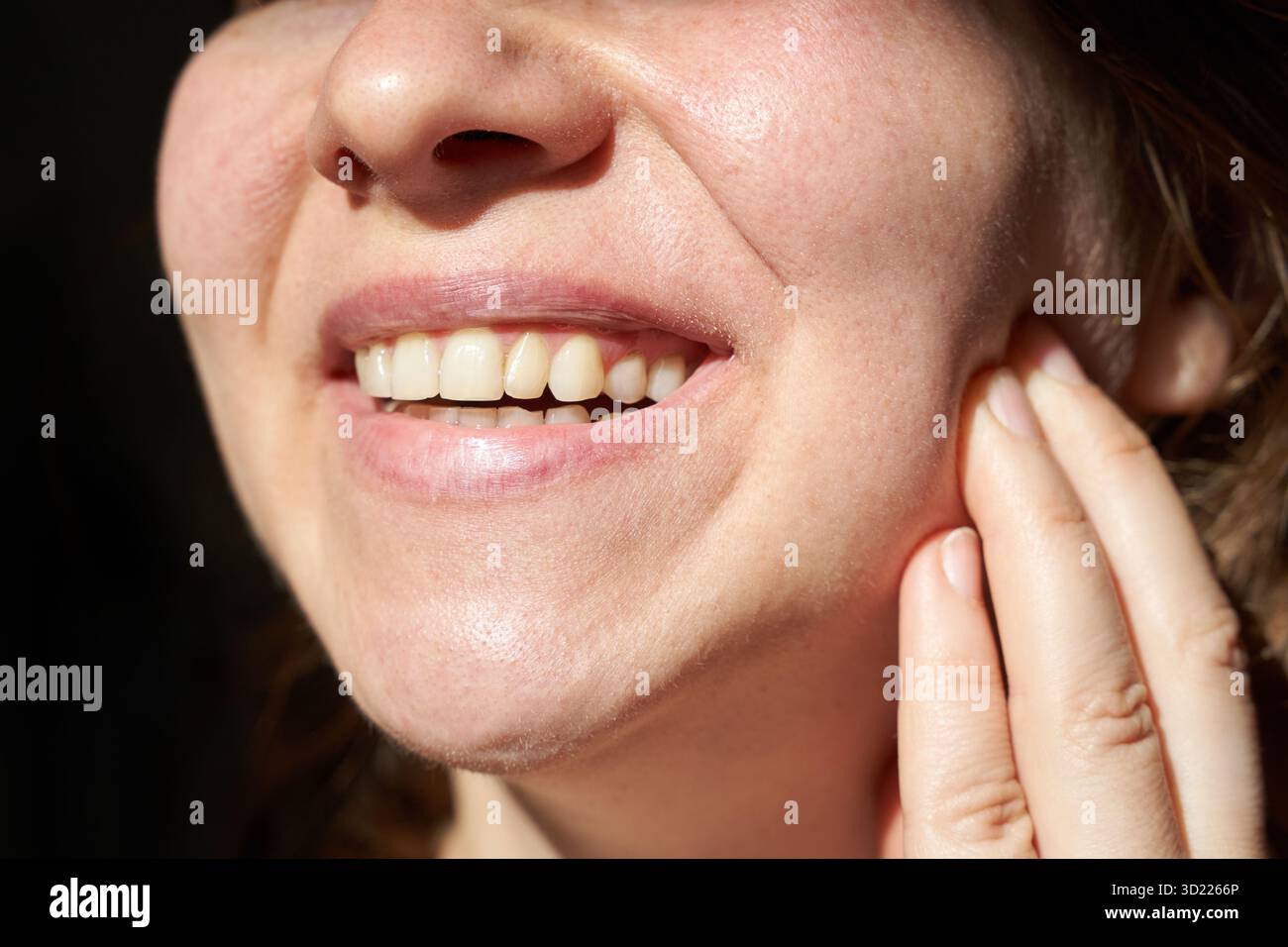Primo piano di giovane donna caucasica sorridente e toccante guancia con denti sani Foto Stock