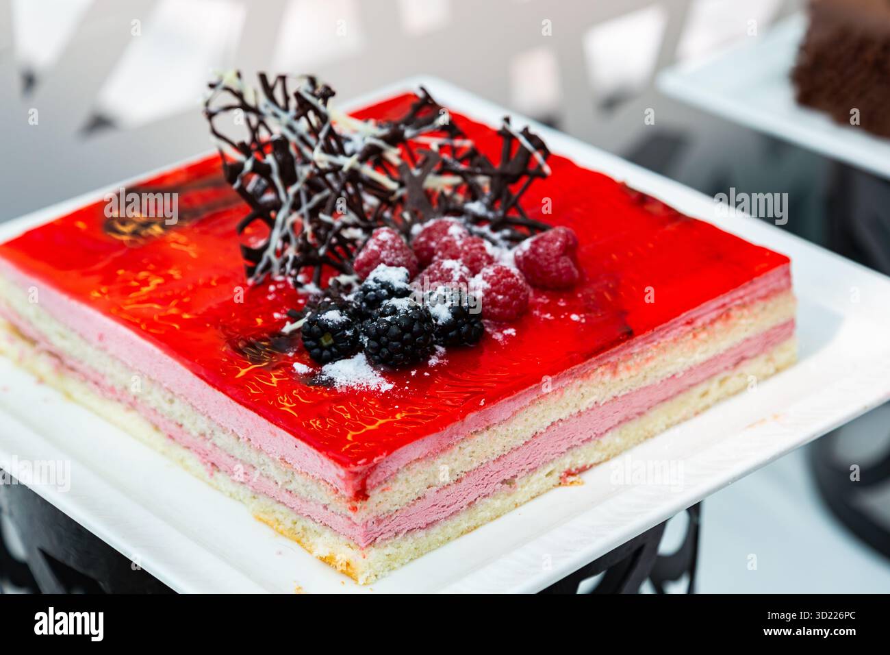 Gli strati di tortino svizzero alla fragola sono decorati splendidamente con crema liscia e ricoperti di ciliegie fresche. Foto Stock