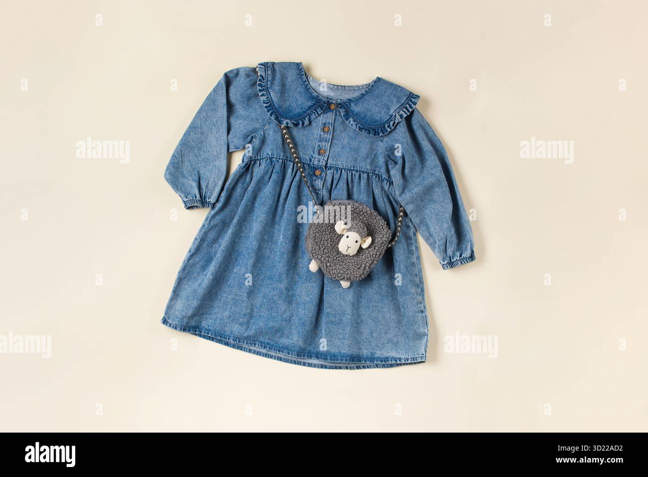 Baby dress in denim su sfondo beige con una graziosa borsa a forma di pecora. Moda per bambini. Disposizione piatta. Foto Stock