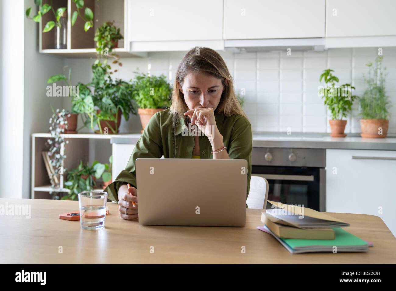 Una donna ansiosa lavora troppo sul laptop, si concentra sullo studio di elearning con libri e documenti a casa Foto Stock