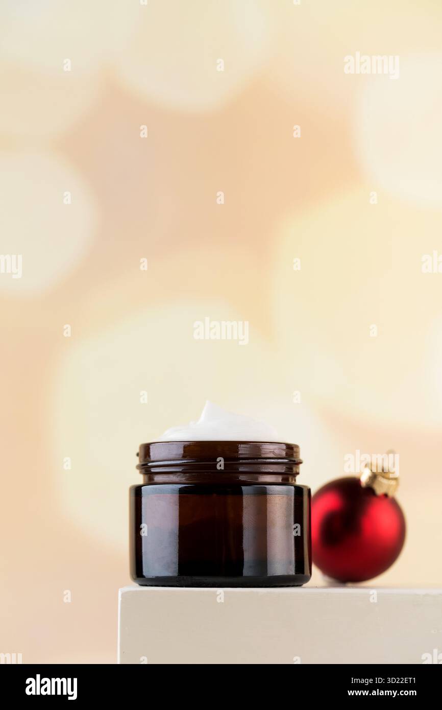Crema nutriente per il viso su un piedistallo con una palla di Natale. Il concetto di cosmetici per la cura della pelle nella stagione invernale. Foto Stock