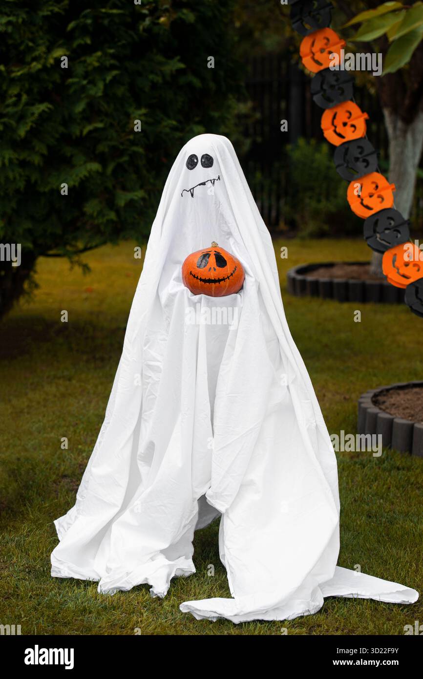 Persona in costume fantasma con zucche spaventose nel cortile Foto Stock