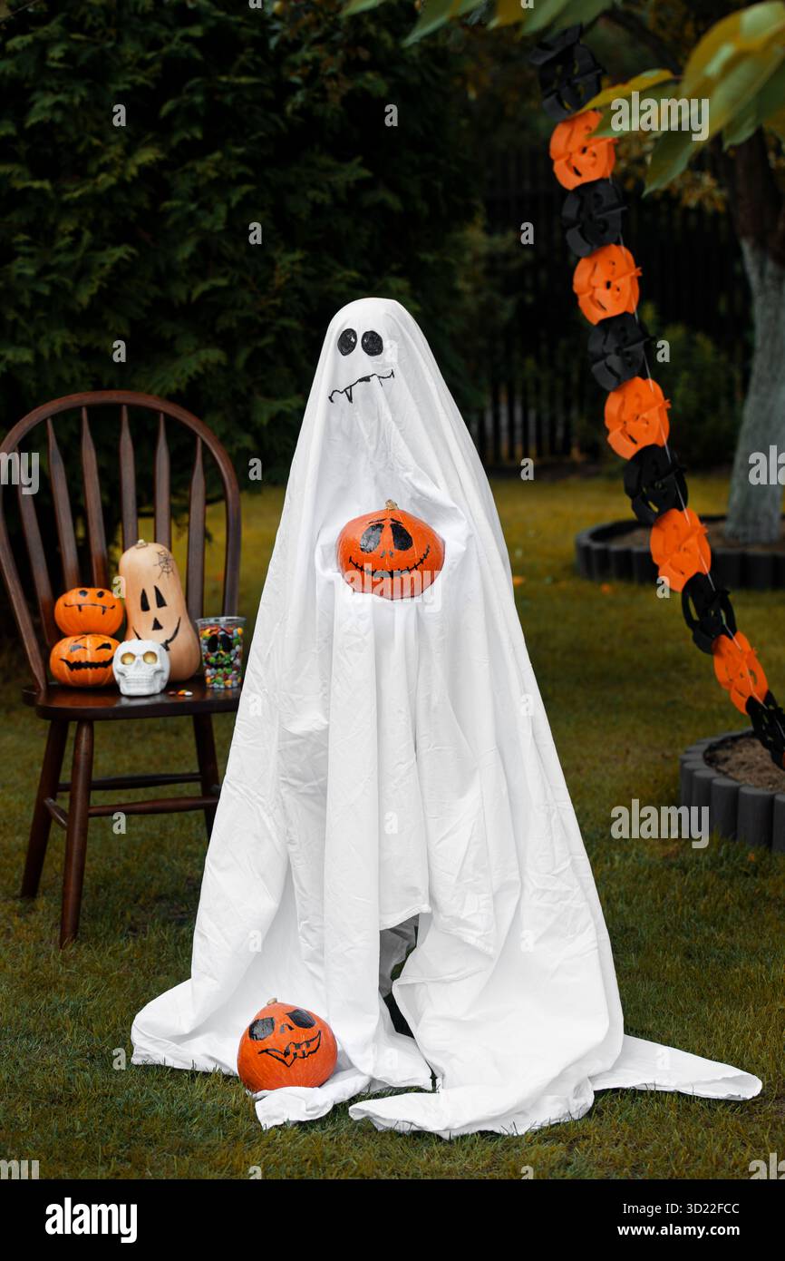 Persona in costume fantasma con zucche spaventose nel cortile Foto Stock