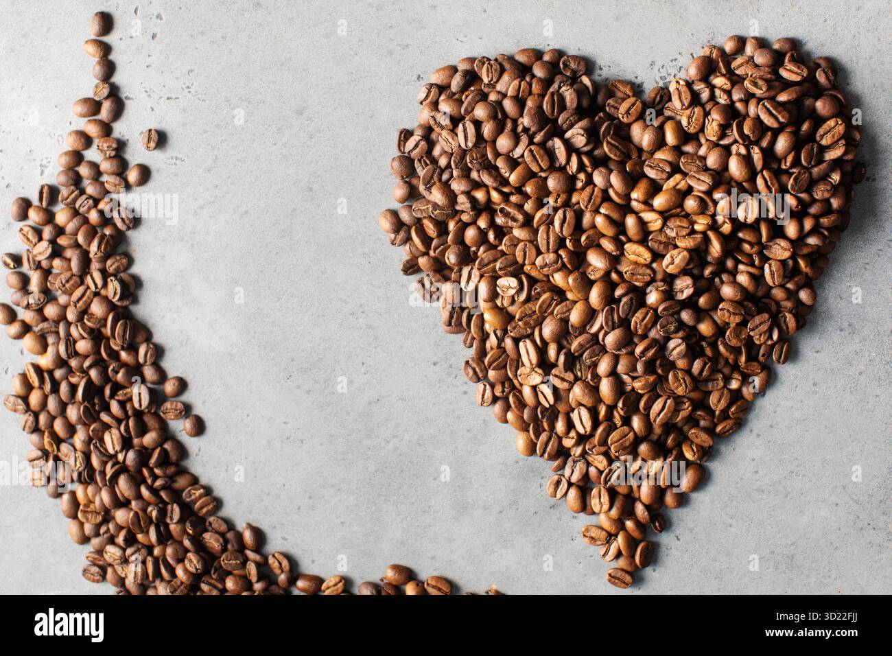 Chicchi di caffè a forma di cuore su sfondo grigio. Foto Stock