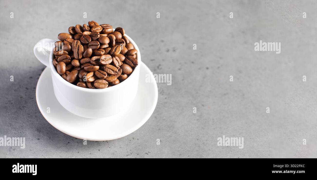 Chicchi di caffè arrosto in una tazza bianca su sfondo grigio. Foto Stock