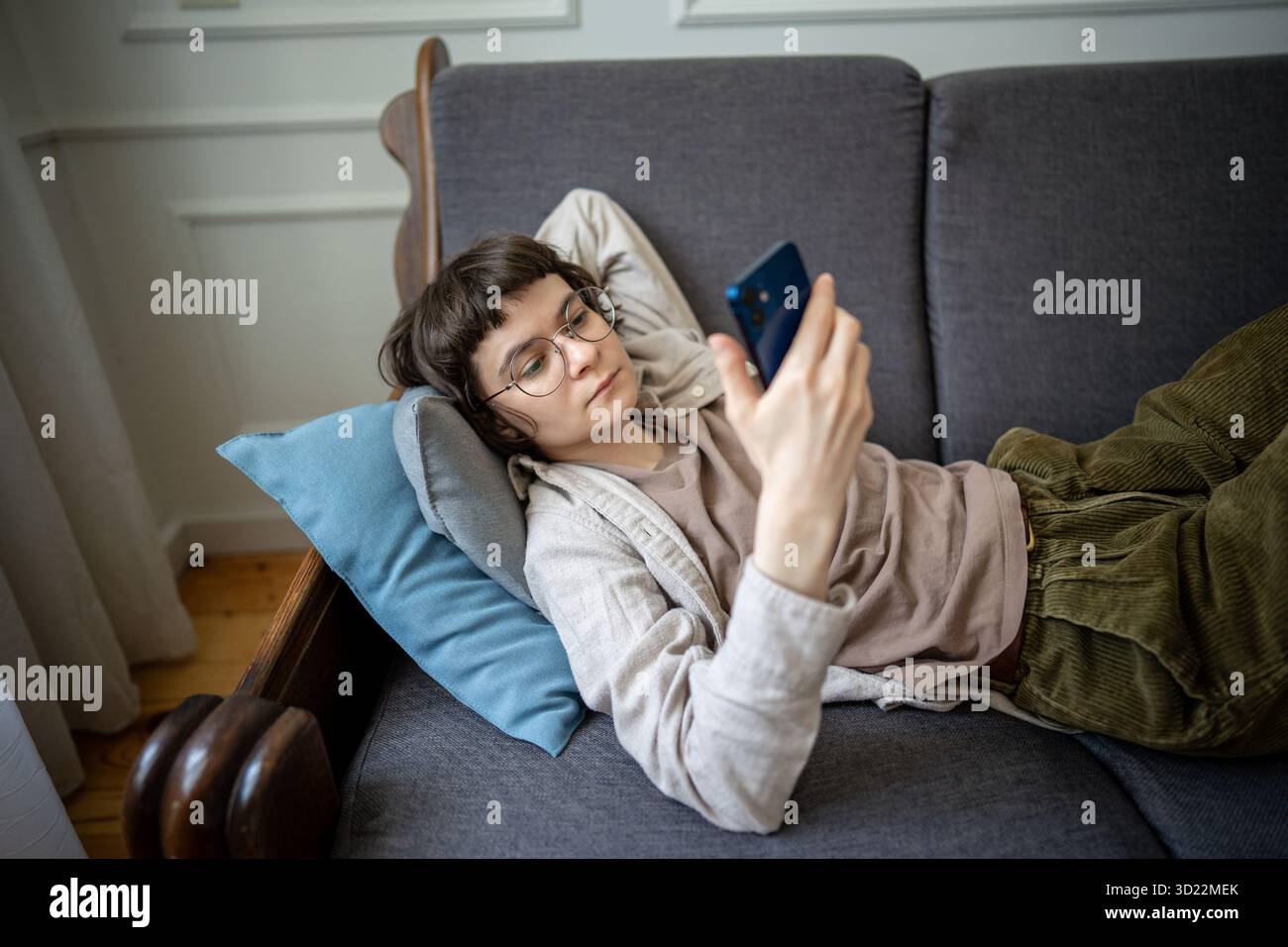 Una donna rilassata che naviga sui social media sullo smartphone mentre si rilassa sul divano con contenuti digitali Foto Stock