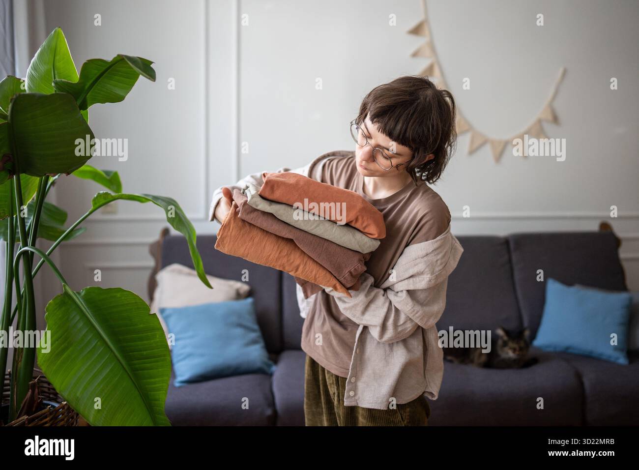 Una giovane donna smista tranquillamente i vestiti da letto appena lavati a casa. Routine di lavanderia, cura dei tessuti Foto Stock