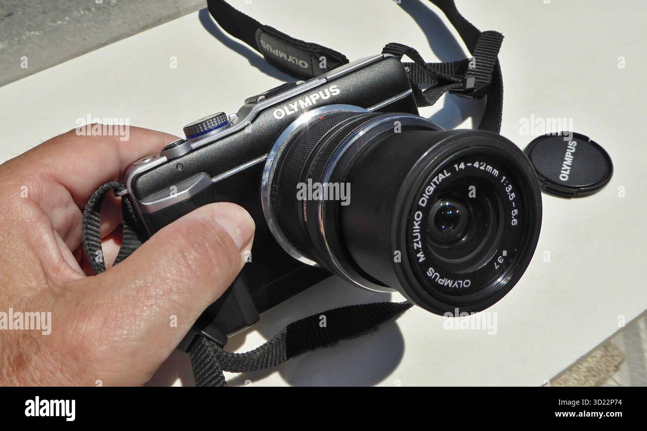 Mano che regge una fotocamera Olympus micro quattro terzi con obiettivo Zuiko e copriobiettivo Foto Stock