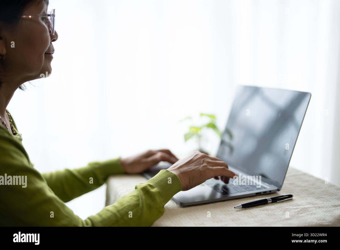 Donna asiatica matura che indossa gli occhiali usando il laptop a casa per il coinvolgimento digitale. Foto Stock