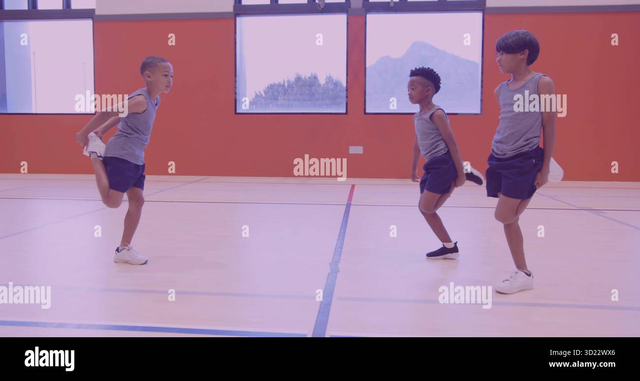 Stretching di 3 ragazzi in equilibrio su un piede tenendo la caviglia nella palestra scolastica indossando magliette grigie senza maniche Foto Stock