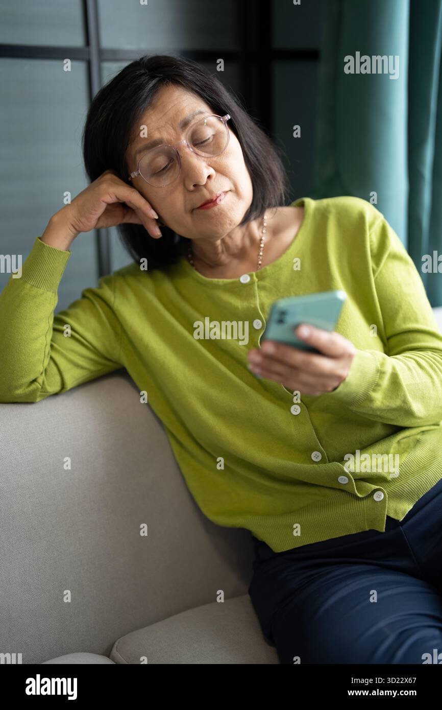 Donna asiatica matura che utilizza smartphone a casa per la connessione digitale Foto Stock