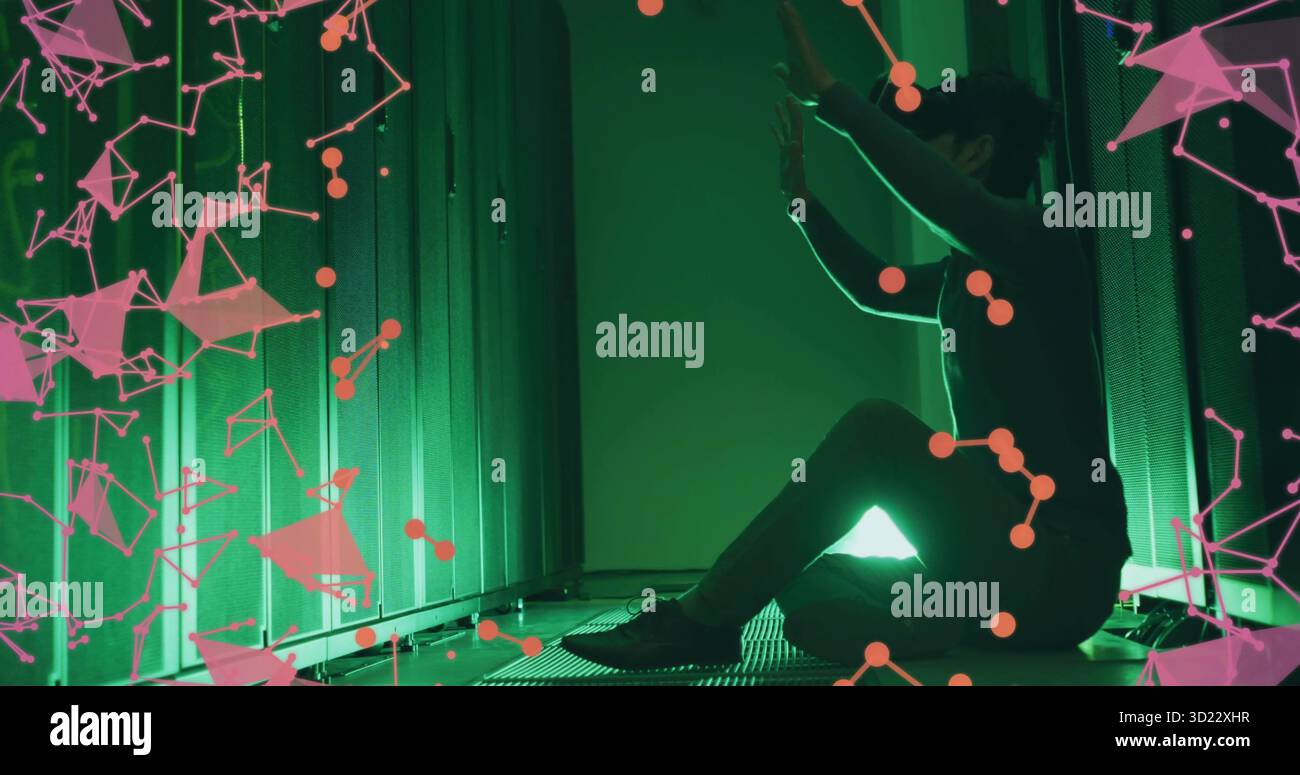 Tecnico inginocchiato in un abito scuro che tocca il server rack con illuminazione verde del data center, mascherina rosa Foto Stock