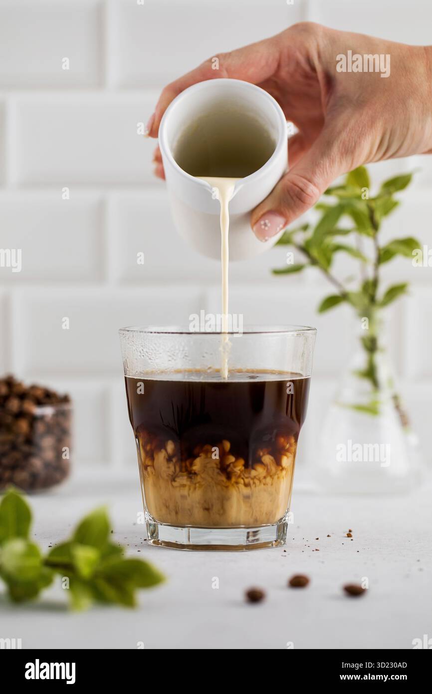 Rinfrescante bicchiere di caffè nero con schiuma leggera, su un moderno sfondo bianco della cucina, perfetto per una mattinata vivace. Foto Stock