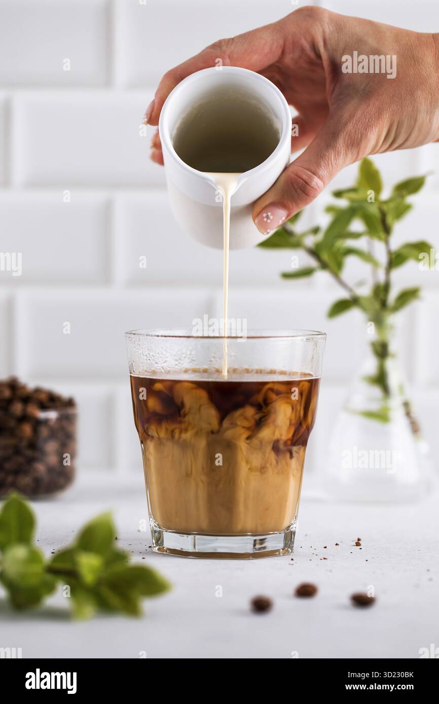 Rinfrescante bicchiere di caffè nero con schiuma leggera, su un moderno sfondo bianco della cucina, perfetto per una mattinata vivace. Foto Stock