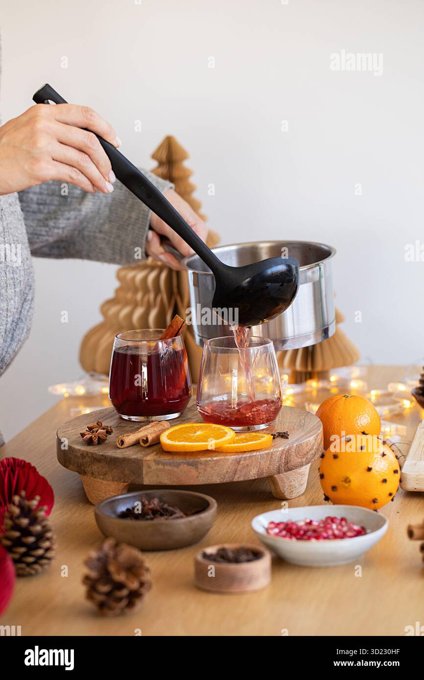Un'accogliente scena natalizia con VIN brulé versato in bicchieri su un tavolo festivo. Foto Stock
