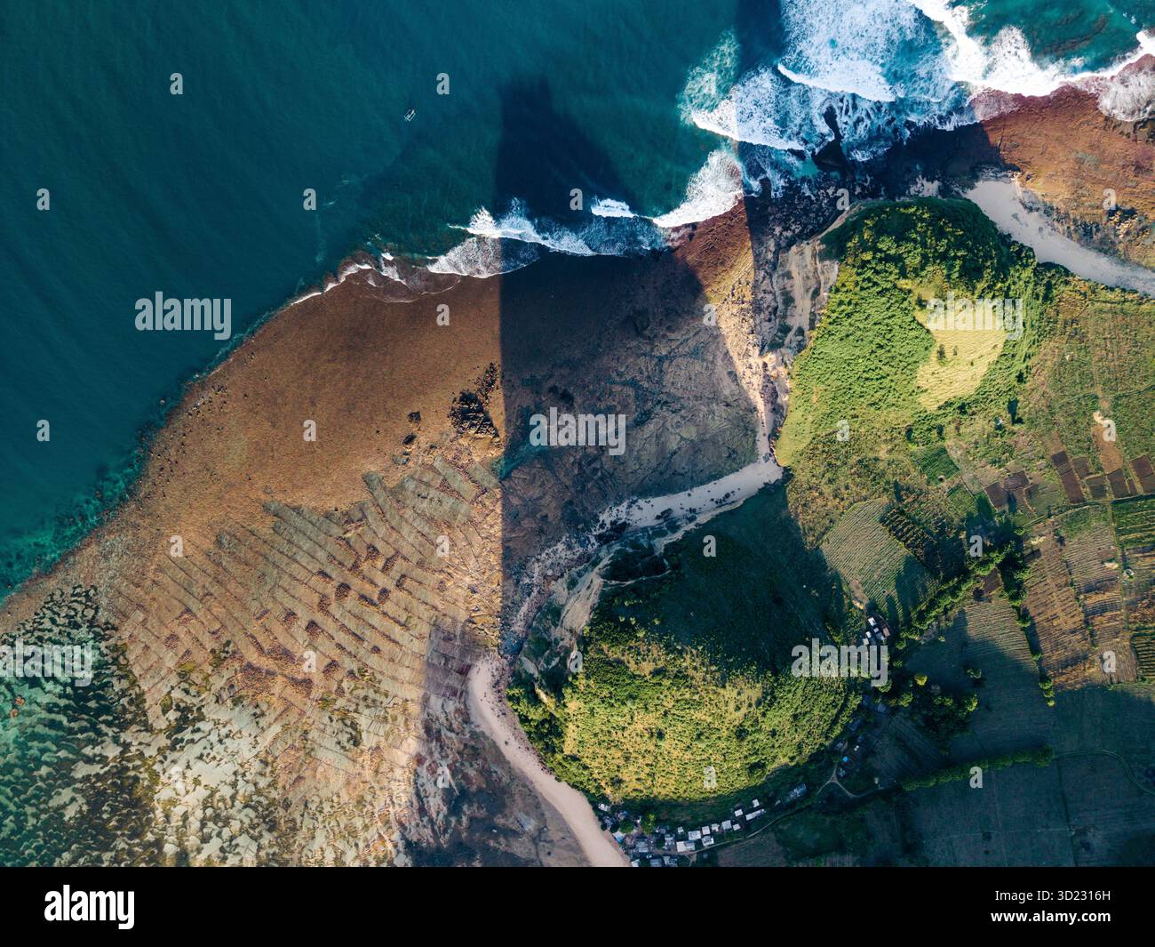 Vista aerea di un vivace paesaggio costiero con onde oceaniche e lussureggianti campi verdi. Lombok, Gerupuk, Indonesia Foto Stock