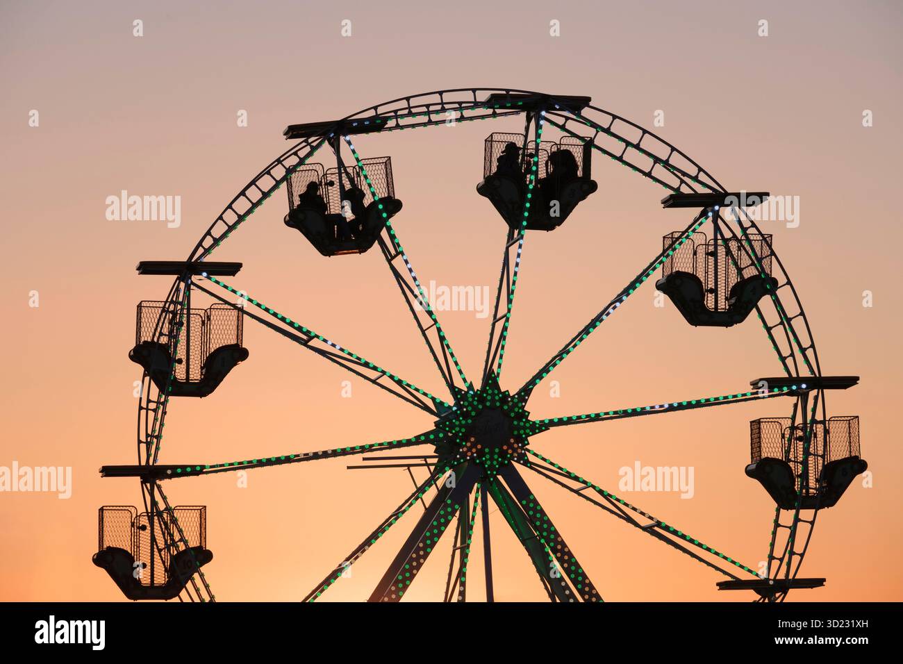 Silhouette di persone che cavalcano una ruota panoramica contro un cielo serale rosa/arancione Foto Stock