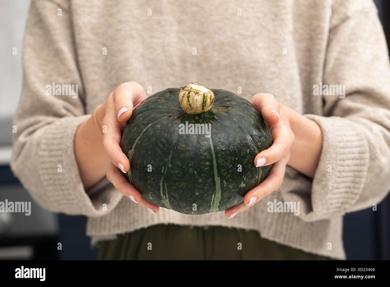 Persona con in mano una zucca verde in abbigliamento casual per il tema del raccolto autunnale Foto Stock