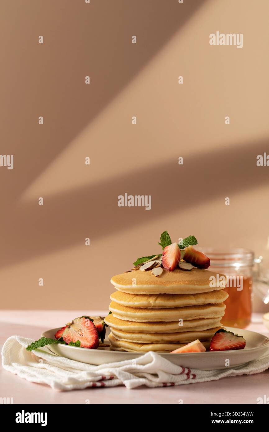 Gusta una deliziosa colazione con frittelle dolci, fragole e miele sotto la calda luce del sole Foto Stock
