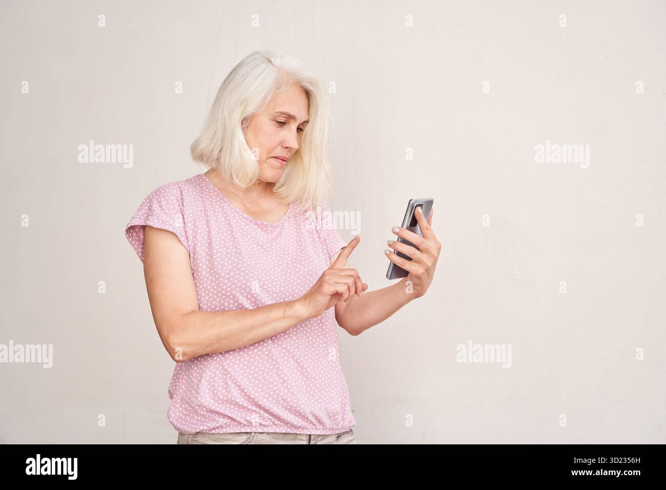 Anziana donna caucasica che utilizza lo smartphone mentre si trova contro il bianco Foto Stock