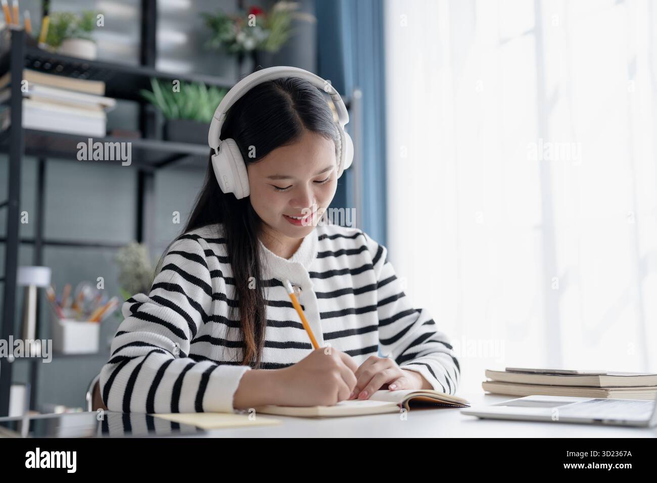 Studentessa asiatica a distanza che prende appunti durante la lezione online con le cuffie Foto Stock