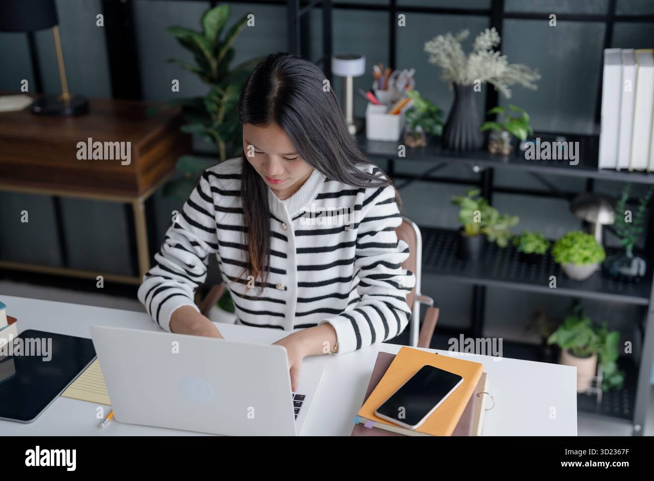 Donna asiatica studentessa impegnata nell'apprendimento online utilizzando il laptop in un ambiente di studio moderno. Foto Stock