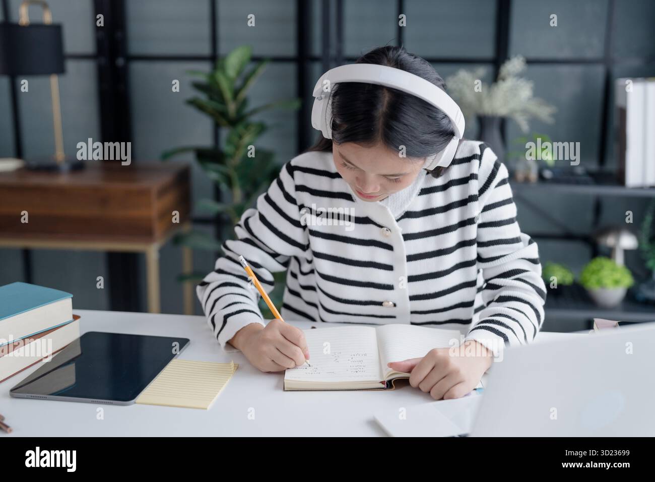 Studentessa asiatica a distanza che prende appunti durante la lezione online con le cuffie Foto Stock